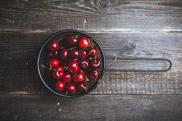 Ripe and juicy cherries in black metal strainer on the dark rustic background. Selective focus....