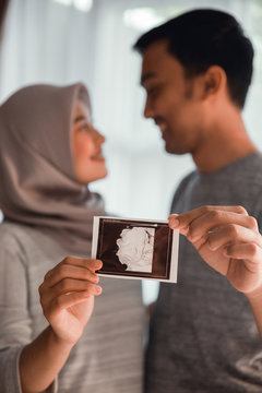 happy muslim couple with ultrasound images on hands. pregnancy at home