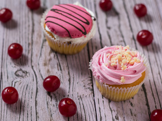 Two fresh cupcakes and scattered cherries on a wooden table.