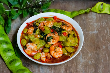 Stir-Fried Twisted Cluster Bean with Shrimps in white dish on wooden table. The Southern Thai food made from Bitter Bean and shrimps.