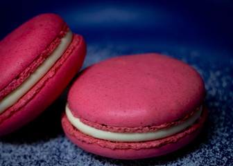 Pink Macaron or Macaroon in blue dish on wooden table. A colorful small and sweet French pastry of made of almond flour and egg whites.