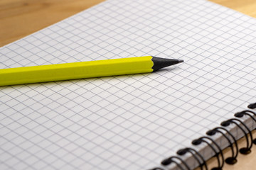 Yellow pencil on a notebook with sheets in a cage on a wooden table. Concept for shopping list, notes, planning. Side view