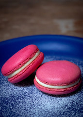 Pink Macaron or Macaroon in blue dish on wooden table. A colorful small and sweet French pastry of made of almond flour and egg whites.