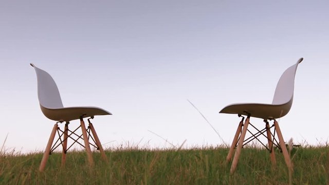 Two facing chairs standing on green grass  isolated against clear blue sky