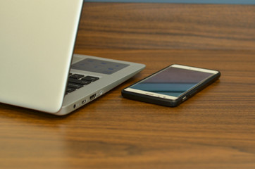 Abstract view of qwerty keyboard and a smart phone in an office setup from the back on a wooden...