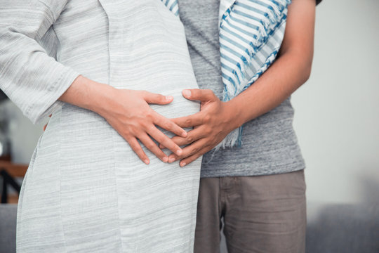 cropped image of asian muslim pregnant woman with her husband hold on tummy at home