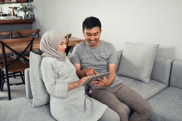 muslim pregnant woman using tablet pc with husband in livingroom