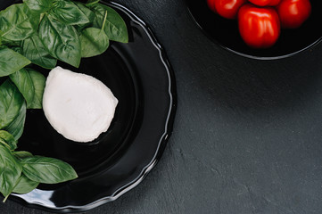 Tomatoes, mozzarella cheese and basil on dark stone background, top view, copyspace. Traditional Italian Caprese Salad, italian mediterranean food.