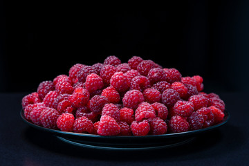 Fresh organic raspberries in a plate on black background