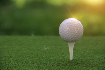Golf ball on tee in beautiful golf course at sunset background.