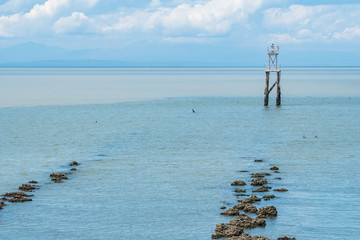 few rocks on the shore stretching to the ocean with a wooden pier on the far end and thick cloud under blue sky over the horizon 