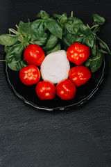Tomatoes, mozzarella cheese and basil on dark stone background, top view, copyspace. Traditional Italian Caprese Salad, italian mediterranean food.