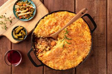 Shepherd's pie in a cooking pan with pickles, herbs, and red wine, overhead shot on a dark rustic...