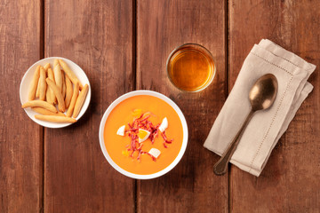 Salmorejo, Spanish cold tomato soup, overhead shot on a dark rustic wooden background with wine and picos, typical breadsticks