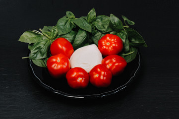 Tomatoes, mozzarella cheese and basil on dark stone background, top view, copyspace. Traditional Italian Caprese Salad, italian mediterranean food.