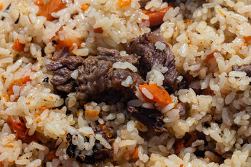 Traditional Eastern culinary dish - pilaf. Close-up view of Asian tasty food background. Ingredients: rice with slices of meat, fat and vegetables (carrot, garlic), spices- popular recipe.