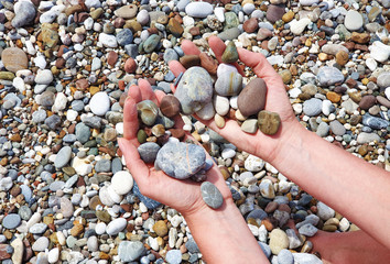 Women's tanned hands holding in the palms of beautiful sea stones on the beach