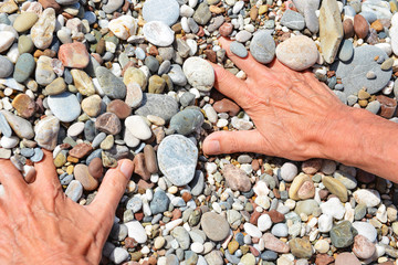 Men's tanned hands lie in the sea pebbles on the beach