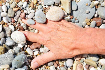 Men's tanned hands lie in the sea pebbles on the beach
