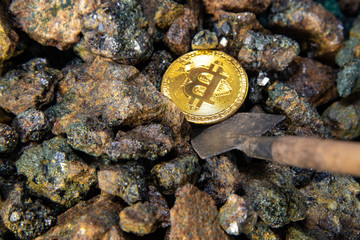 Top view close-up of a bitcoin stack of gold coins on a background of stones with a shovel. Cryptocurrency mining concept