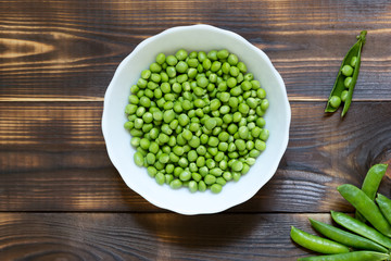 Healthy eating concept. Fresh green peas in white plate on dark wooden table.