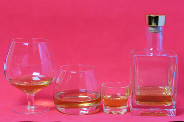 A bottle of strong alcohol. Glasses and a stack with a strong alcoholic beverage poured into them. Stand in a row. Against the background of coral color.