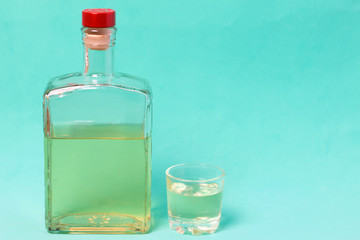 A bottle of strong alcohol. From transparent glass, a square form with a red stopper. Near a stack...