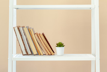 White bookshelf with  books and stationery against beige wall