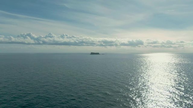 Slow aerial flight towards the island of Filfla off the coast of Malta in the Mediterranean ocean following the glistening setting sun.