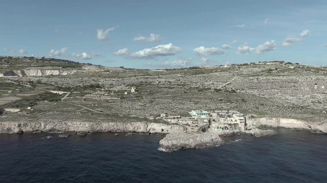 Slow forward-facing aerial over the Mediterranean with a downwards panning reveal of the fishing village of Ghar Lapsi