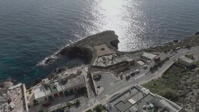Forward aerial birds-eye view of the popular village of Ghar Lapsi in Malta with late afternoon sun glistening off of the Mediterranean