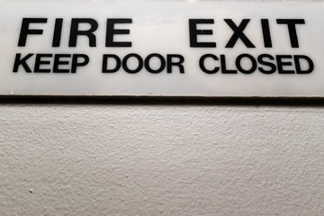 Obraz premium Fire exit keep door closed sign. Well lit white sign with strong black font on a white wall.