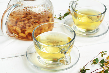Glass kettle and cup of herbal tea on white wooden background