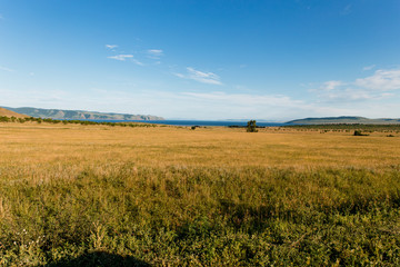 Fototapeta premium Blue sky with white clouds, trees, fields and meadows with green grass, against the mountains. Composition of nature. Rural summer landscape.
