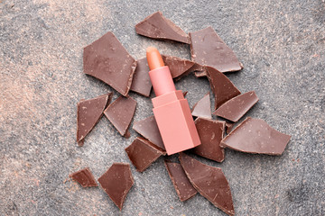 Lipstick with chocolate pieces on grey background