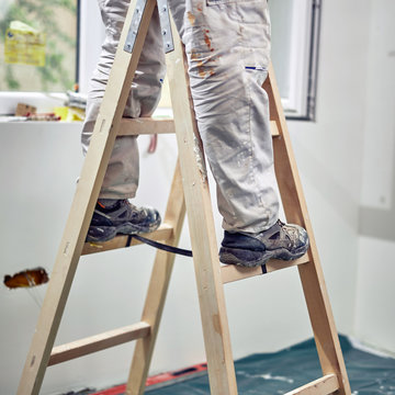 Worker standing on the ladder and renovating house.