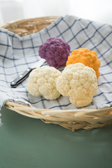 Bunter Blumenkohl in Lila, Orange und Weiß auf Geschirrtuch mit Messer in Korb auf Pastell Mint Grün Hintergrund