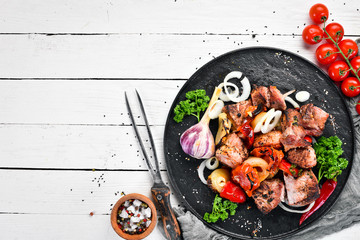 Kebab in a plate. Baked meat with onions and tomatoes. Barbecue. Top view. Free space for your text. Rustic style.