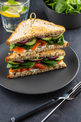 Sandwiches with cream cheese, salmon and spinach on a dark background.