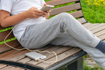 Boy using phone on the bench while charging from the power bank.