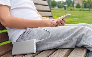 Boy using phone on the bench while charging from the power bank.
