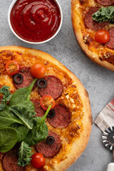Tasty pepperoni pizza and cooking ingredients tomatoes basil on grey concrete background. Top view of hot pepperoni pizza. With copy space for text.
