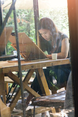 Beautiful woman embodying her ideas on paper with help of paintbrush and watercolors, interior of coffee cafe on natural background.