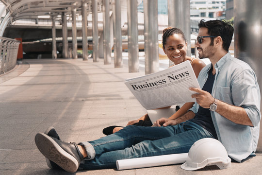 diversity of business partners with business newspaper on hands having business conversation during relaxing sitting on pathway outdoor