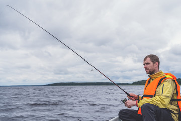 Fisherman sitting in an old wooden boat and fishing on a cloudy day.