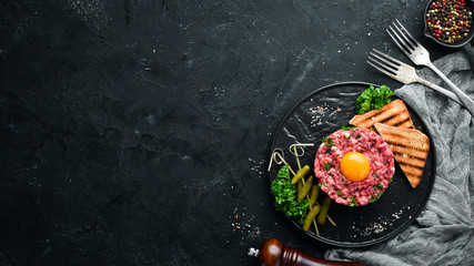 Beef steak tartare with raw egg yolk, pickled cucumber and onions. French cuisine. Top view. Free...
