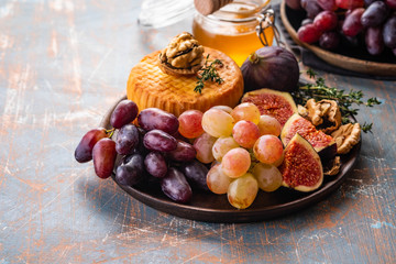 Cheese plate served with grapes, jam, figs, crackers and nuts on a background.