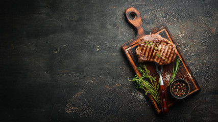 Grilled ribeye beef steak, herbs and spices on a dark table. Top view. Free space for your text.