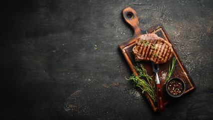 Foto op Plexiglas Grilled ribeye beef steak, herbs and spices on a dark table. Top view. Free space for your text. © Yaruniv-Studio