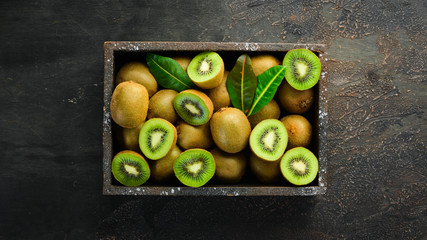 Fresh kiwi and green leaves in a wooden box on the old background. Fruits. Top view. Free space for text.